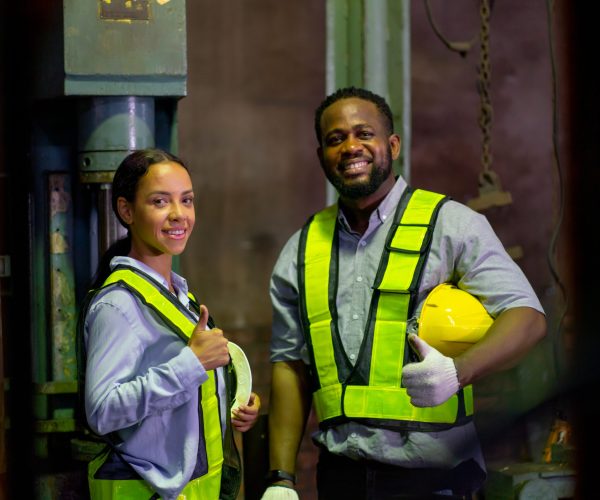 African American woman smile and look at camera also stand near her coworker hold hard hat after finish work in industrial workplace area.