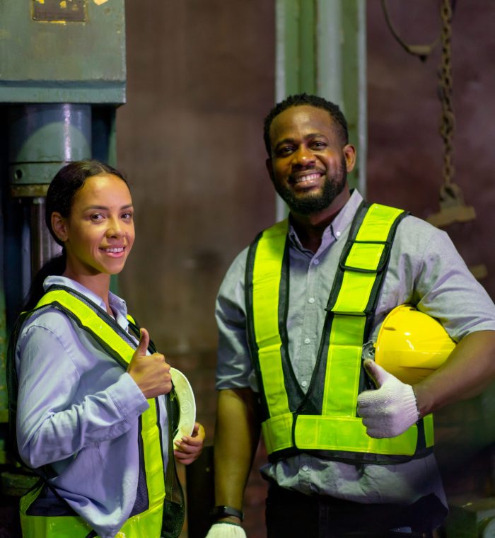 African American woman smile and look at camera also stand near her coworker hold hard hat after finish work in industrial workplace area.