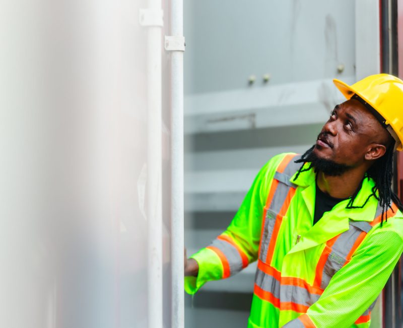 Industrial workers conducting container inspections inside a shipping facility. Reviewing documents and using a handheld device to ensure accuracy in logistics, transportation, and cargo management.