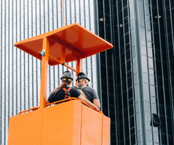 Workers in a construction cradle climb on a crane to a large glass building.The crane lifts the workers in the car seat.Construction.