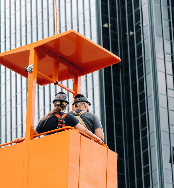 Workers in a construction cradle climb on a crane to a large glass building.The crane lifts the workers in the car seat.Construction.